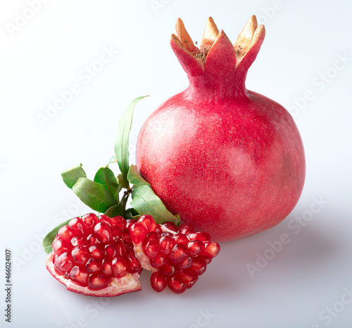 Two pieces of a beautiful young juicy pomegranate with beautiful transparent pomegranate seeds and a whole pomegranate with a crown in a beautiful red peel with young fresh pomegranate leaves