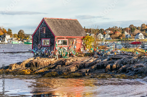 Fotografie, Tablou An old shake shingled lobster shack is festooned with many floats and other fishing paraphernalia on the rocky shore of Mackerel Cove on Bailey Island, Harpswell, Maine