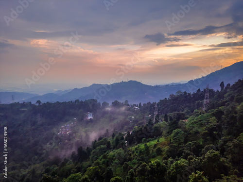 dramatic sunset orange sky over mountain range and green forest at evening from hill top