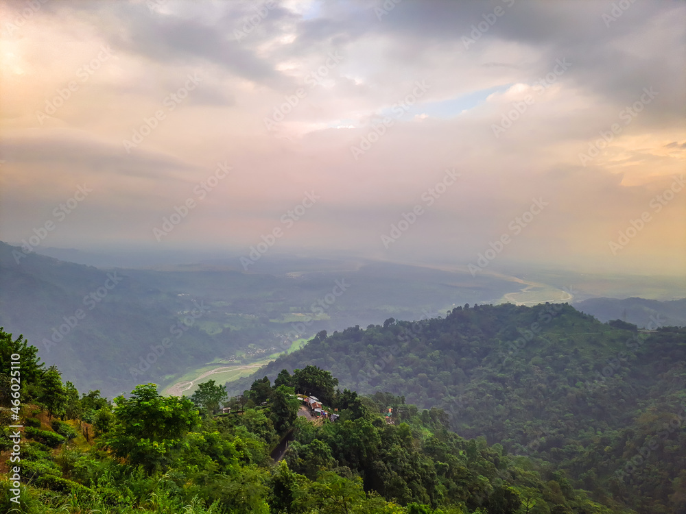 dramatic sunset orange sky over mountain range and green forest at evening from hill top