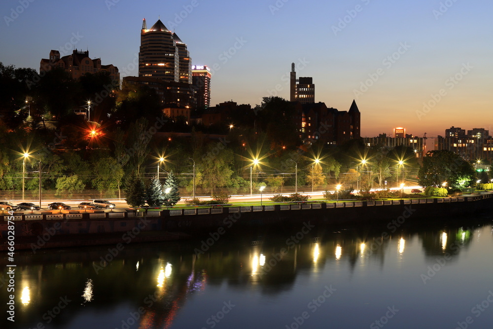 Scenic view of beautiful modern buildings, skyscrapers and towers of night big city are reflected in the Dnieper River in evening. Dnipro, Dnepropetrovsk, Ukraine