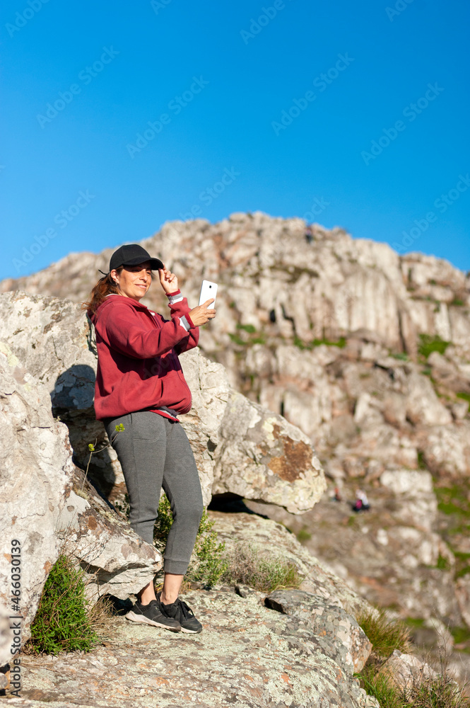 young woman above the mountains in the middle of nature taking photos of the landscape and likewise with a sunny day.