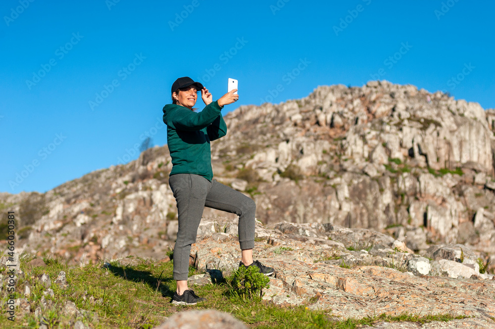 young woman above the mountains in the middle of nature taking photos of the landscape and likewise with a sunny day.