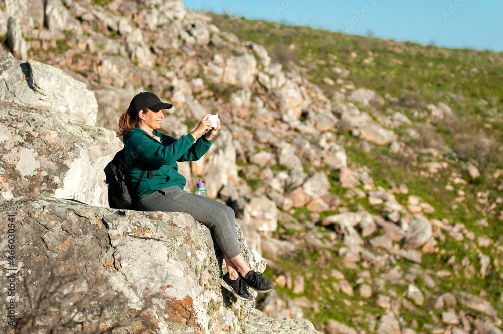 young woman above the mountains in the middle of nature taking photos of the landscape and likewise with a sunny day.