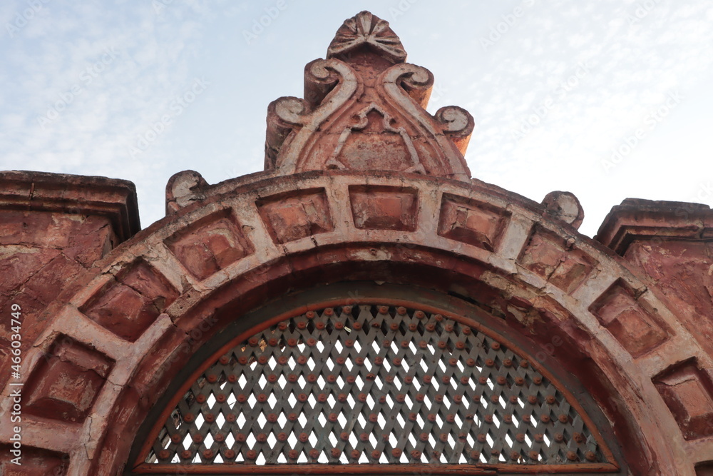 Brick arch of an old building with a lattice on a blue sky background.