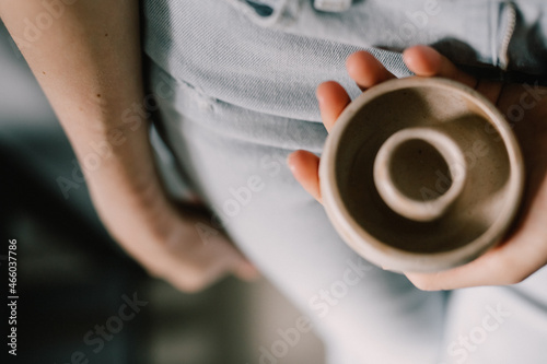 Women's beautiful hands hold a pottery product - a small cup made of clay. Pottery master's workshop. concept is a manual hobby.