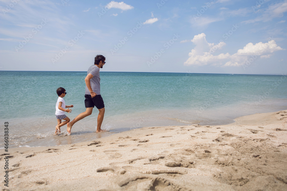 father in a striped T-shirt walks with his son in shorts and a T-shirt walking on beach in summer during a vacation