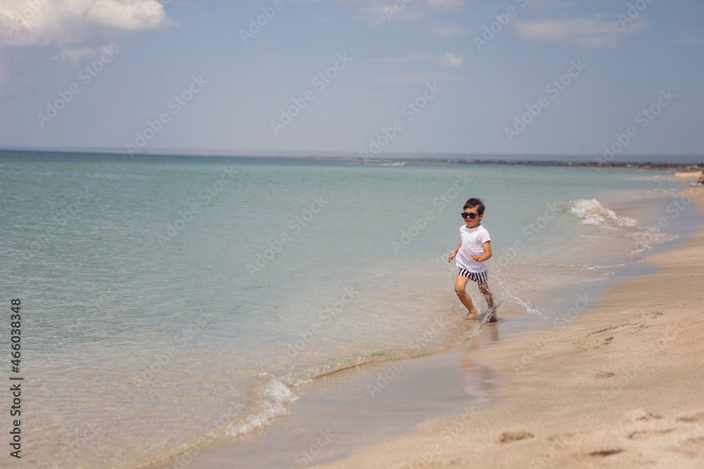 boy child in striped shorts and a white T-shirt walks on sandy beach and in sunglasses boy child in striped shorts and a white T-shirt walks on sandy beach and in sunglasses