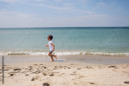 boy child in striped shorts and a white T-shirt walks on sandy beach and in sunglasses