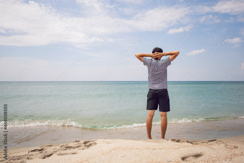 guy in striped T-shirt and shorts is standing on the beach and spread his arms to the side