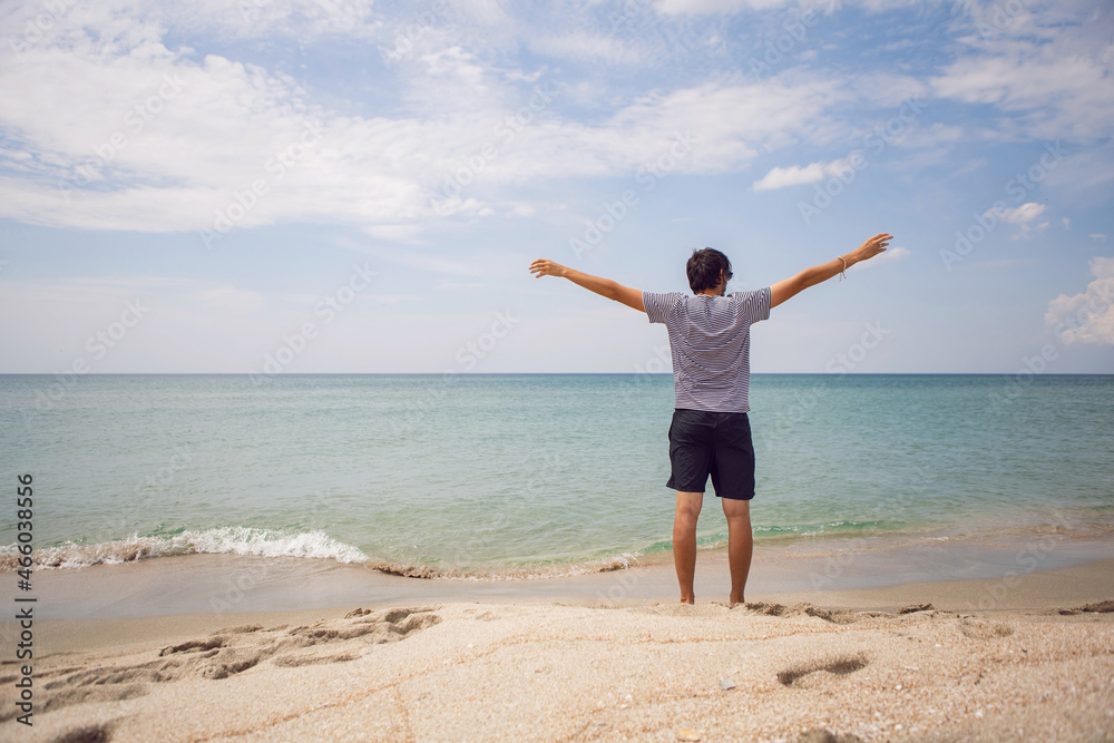 guy in striped T-shirt and shorts is standing on the beach and spread his arms to the side guy in striped T-shirt and shorts is standing on the beach and spread his arms to the side