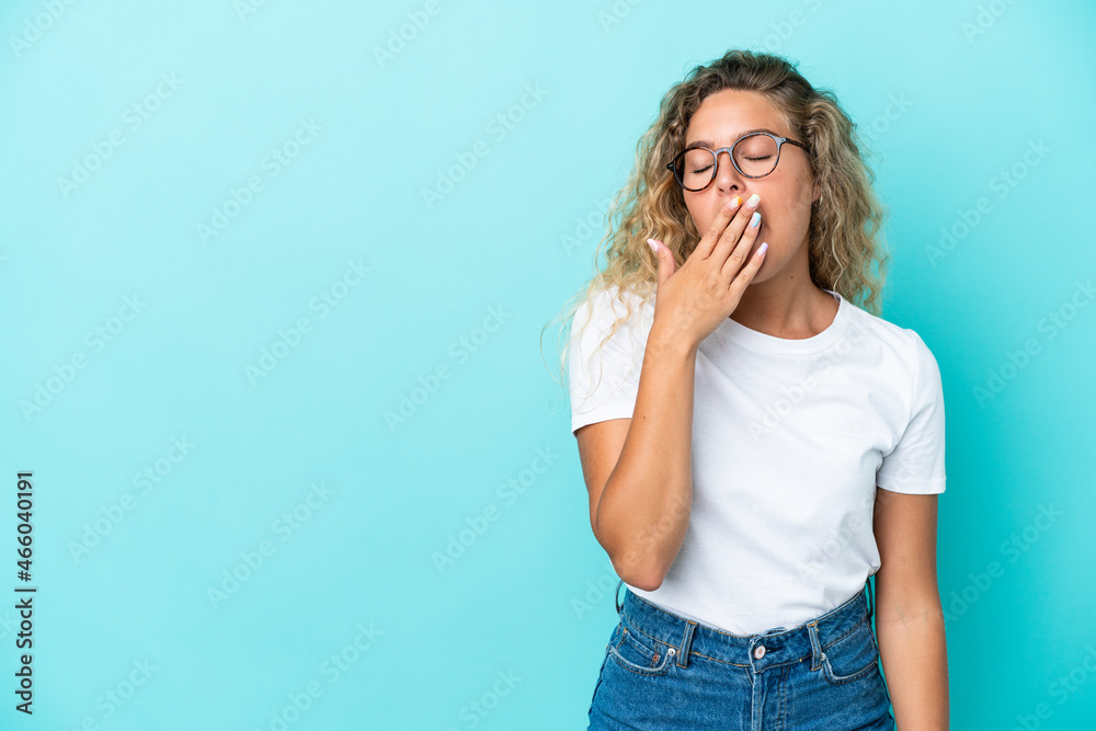 Girl with curly hair isolated on blue background yawning and covering wide open mouth with hand Girl with curly hair isolated on blue background yawning and covering wide open mouth with hand