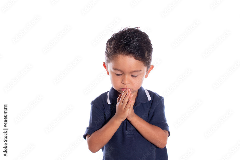 Latin boy praying with closed eyes, isolated on white background. Religious concept. Child praying.