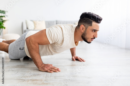 Millennial Arab man doing push ups, standing in plank pose, doing strength exercises at home. Domestic workout concept