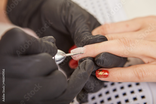 Manicurist removing cuticle on female hand with electric nail drill