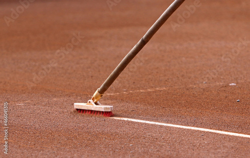 Cleaning the marking line of the clay tennis court with special brush. Clay tennis court cleaning. Maintenance and preparation surface of orange sport ground for game. Copy space photo