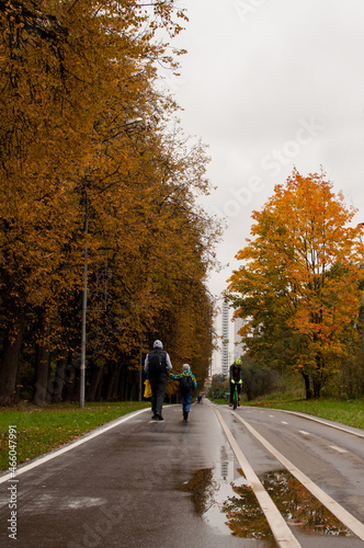 a cyclist, a man and a child move in an autumn park along a marked road