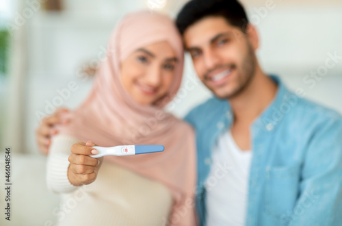 Closeup of positive pregnancy test in muslim woman hands cuddling with her husband and smiling to camera