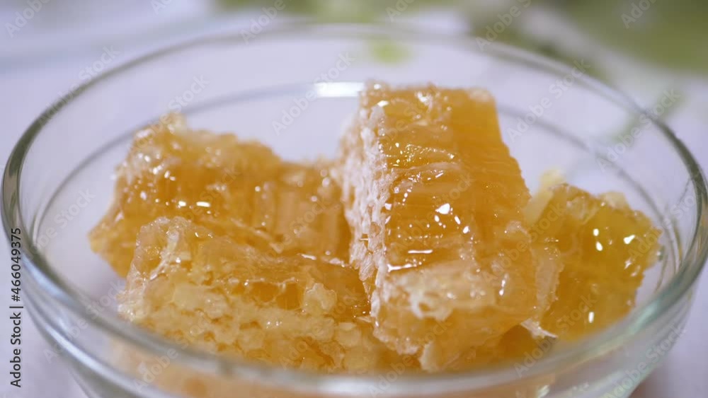 Dense Natural Honey Flows in a Thick Layer in a Glass Bowl on a Honeycomb. Orange transparent, melting, liquid honey flows drip over the bee combs. Healing, organic, healthy beekeeping product. Zoom.