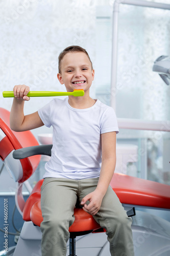 little boy child laughs at a dentist appointment. boy shows how to brush his teeth with a big green toothbrush. Concept - checking caries in children
