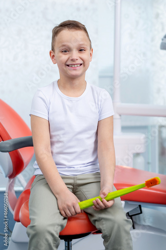 A little boy child laughs at a dentist appointment. boy is holding large green toothbrush in his hands. Concept - checking caries in children