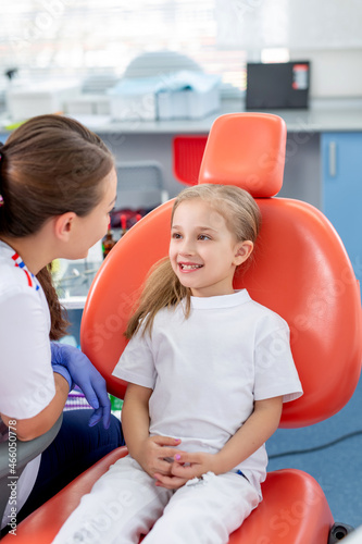 pediatric dentist talks to a little girl and tells her how to take care of her teeth. beautiful girl is smiling in dentist s office. concept is a children s medical examination.