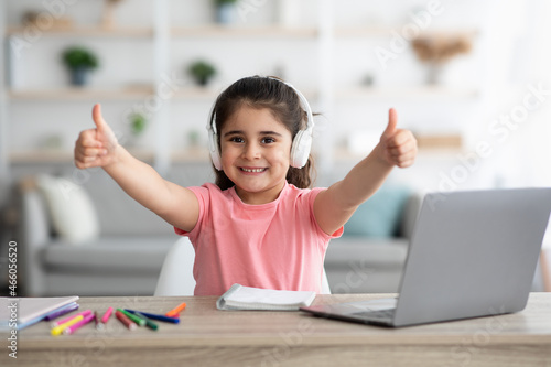 Little Arab Schoolgirl Showing Thumbs Up While Study With Laptop At Home photo