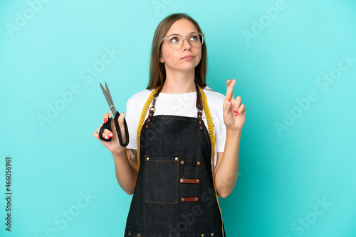 Young Lithuanian seamstress woman isolated on blue background with fingers crossing and wishing the best