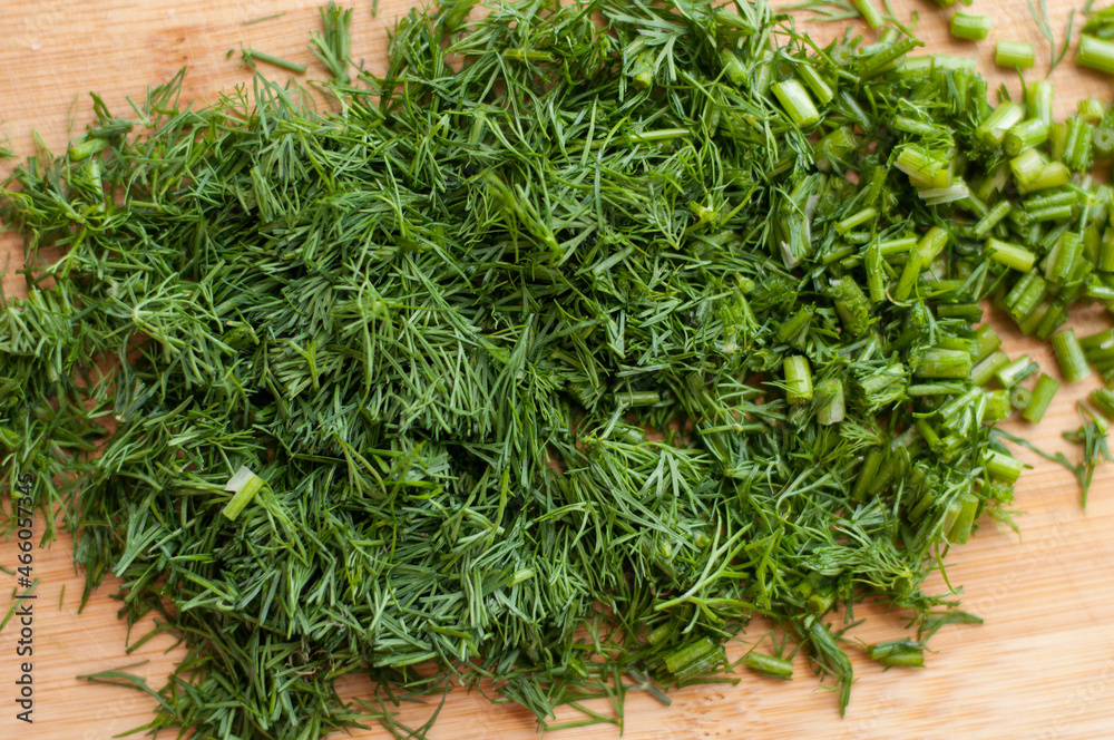 Finely chopped fresh dill on a wooden cutting board with blurred edges and a solid background Finely chopped fresh dill on a wooden cutting board with blurred edges and a solid background