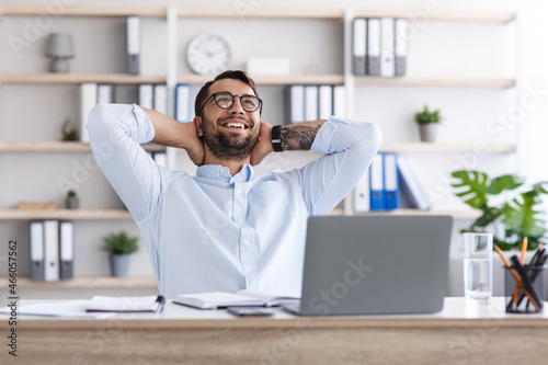 Satisfied middle aged caucasian guy with beard in glasses resting from work at laptop