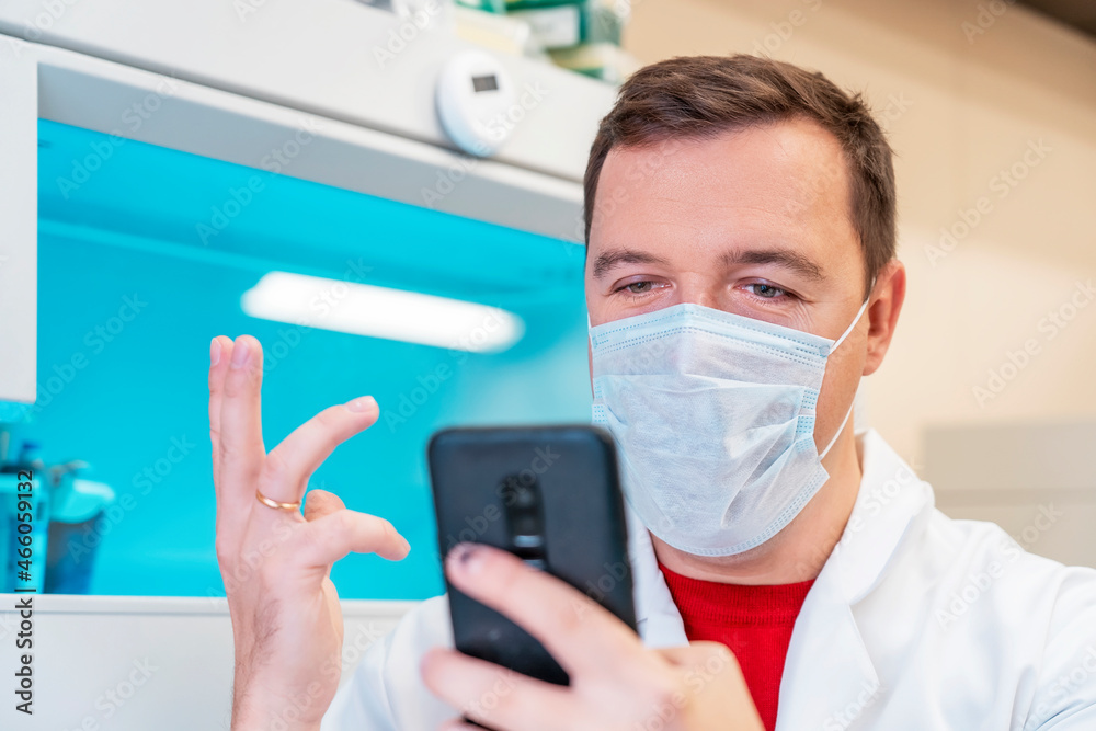 Excited scientist wearing white coat showing emotions of joy about victory in online lottery in room with laboratory box in UV ligh. Amazed male in medical mask win money celebration success and sit Excited scientist wearing white coat showing emotions of joy about victory in online lottery in room with laboratory box in UV ligh. Amazed male in medical mask win money celebration success and sit