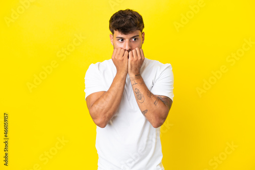 Young caucasian handsome man isolated on yellow background nervous and scared putting hands to mouth © luismolinero
