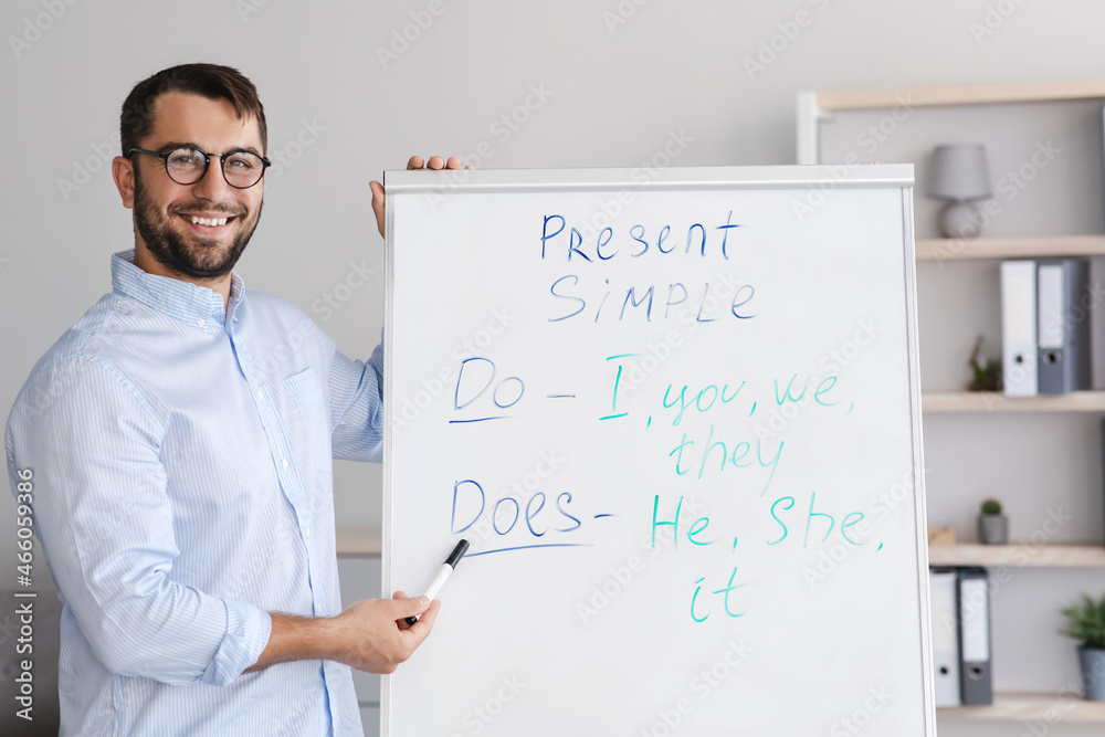 Friendly happy mature caucasian man teacher in glasses shooting online lesson pointing to blackboard in living room Friendly happy mature caucasian man teacher in glasses shooting online lesson pointing to blackboard in living room