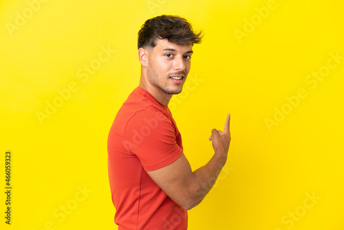 Young caucasian handsome man isolated on yellow background pointing back