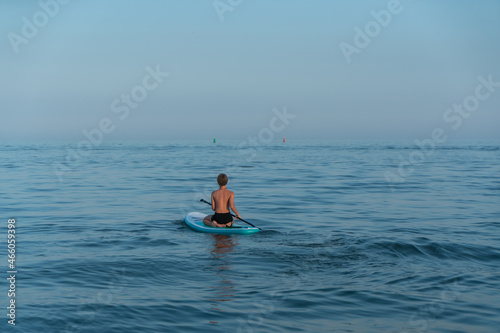 A boy of 11 years old swims on a SUP board in the sea after sunset. © Виктор Кеталь