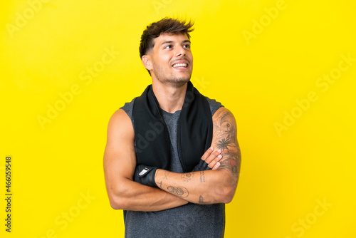 Young sport caucasian man with towel isolated on yellow background looking up while smiling