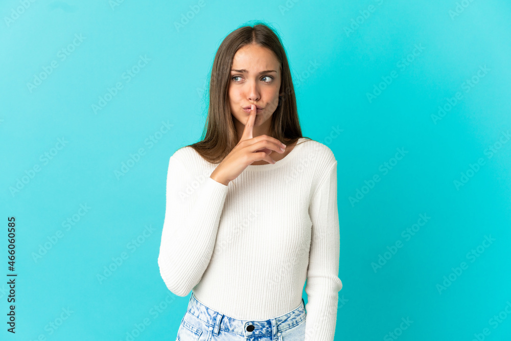 Young woman over isolated blue background showing a sign of silence gesture putting finger in mouth Young woman over isolated blue background showing a sign of silence gesture putting finger in mouth