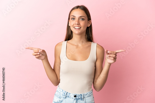 Young woman over isolated pink background pointing finger to the laterals and happy