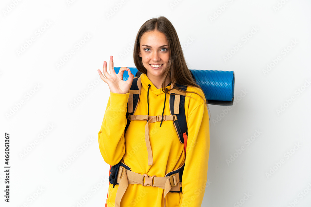 Young mountaineer woman with a big backpack over isolated white background showing ok sign with fingers Young mountaineer woman with a big backpack over isolated white background showing ok sign with fingers