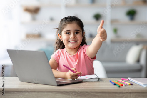 Little Arab Girl Showing Thumb Up While Study With Laptop At Home photo