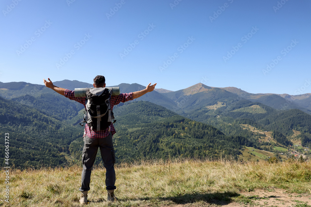 Happy man with backpack and camping mat in mountains on sunny day, back view