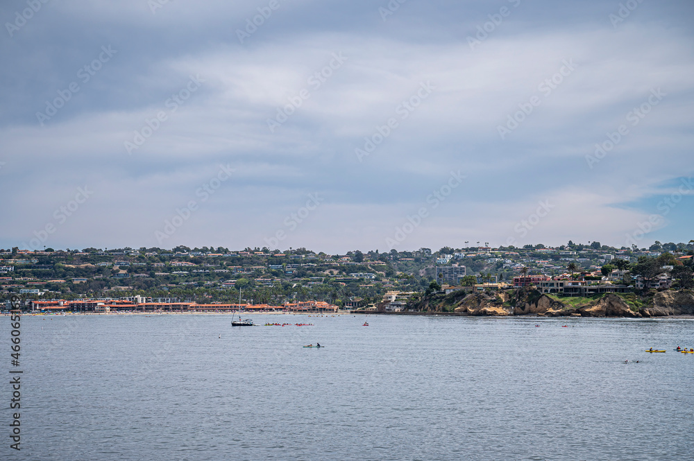 La Jolla, California, USA - October 3, 2021: Wide veiw from Point La Jolla on red roofed beach and tennis club along water with green belt of housing separating blue cloudscape from ocean.