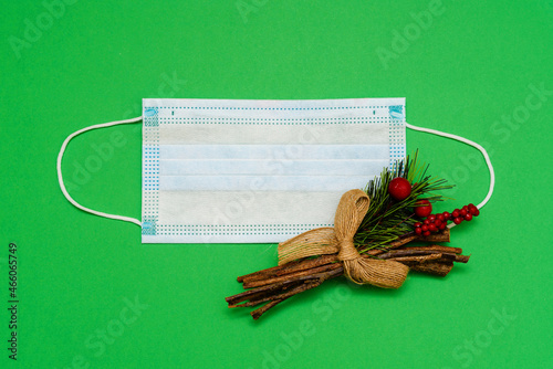 A medical mask on green background with spruce branch. Top view with copy space, space for text. Celebrating the New Year. Happy New Year 2022 concept.