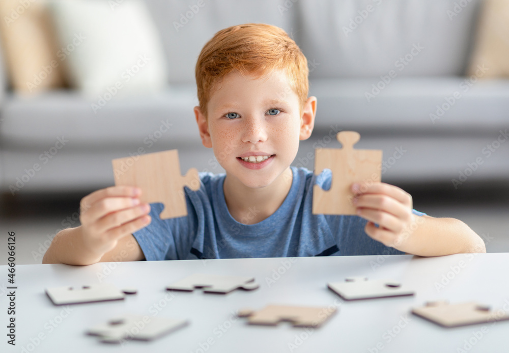 Joyful preteen boy holding two pieces of wooden puzzles Joyful preteen boy holding two pieces of wooden puzzles