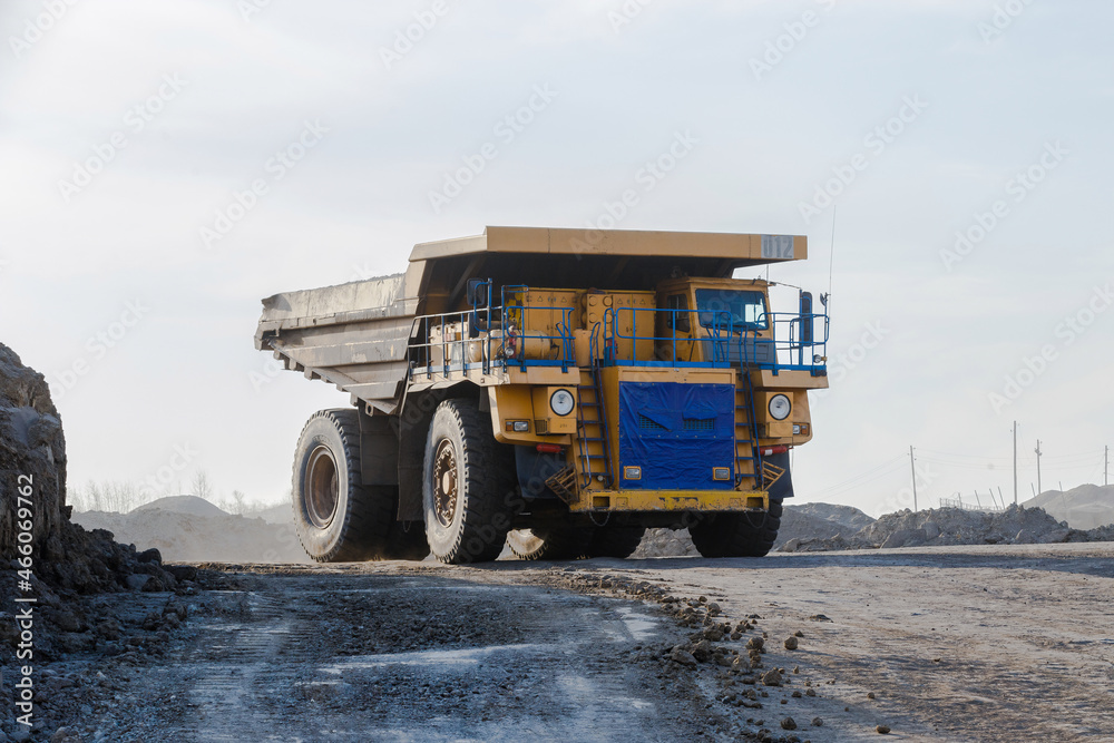 Industrial work in an open pit coal mine. A large yellow dump truck is carrying coal soil through the quarry. Open pit coal mining. Industrial work in an open pit coal mine. A large yellow dump truck is carrying coal soil through the quarry. Open pit coal mining.