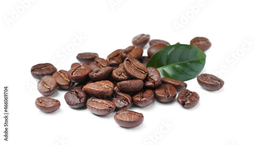Pile of roasted coffee beans with fresh leaf on white background