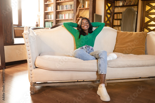 Relaxed black woman leaning back on couch with closed eyes, resting on comfy sofa in living room, copy space