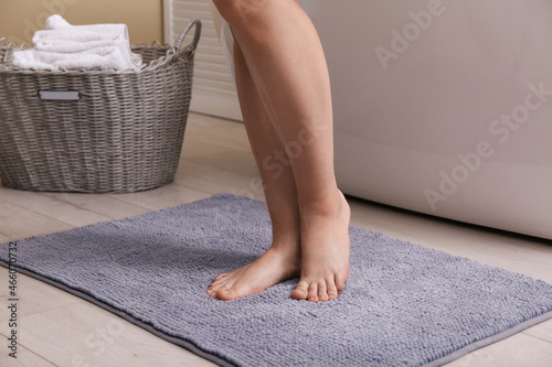 Woman standing on soft grey bath mat near tub at home, closeup