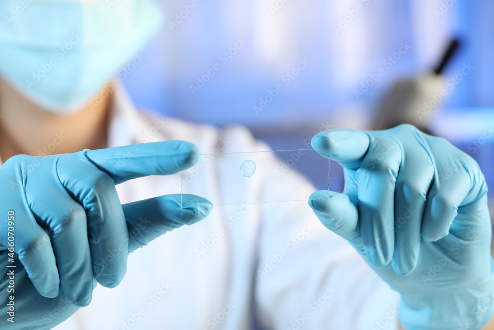 Scientist holding microscope slide with light blue sample in laboratory, closeup Scientist holding microscope slide with light blue sample in laboratory, closeup
