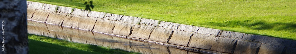 Fototapeta premium Narrow canal in public park with green grass meadow riverbank gutter banner